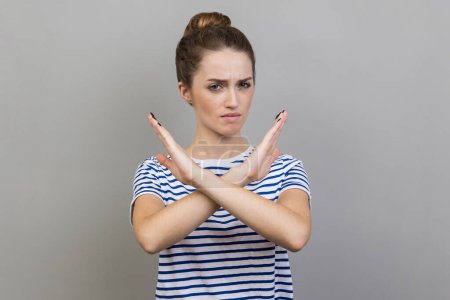Photo for No way, absolutely not. Portrait of woman wearing striped T-shirt showing x sign with crossed hands, meaning stop, this is the end. Indoor studio shot isolated on gray background. - Royalty Free Image