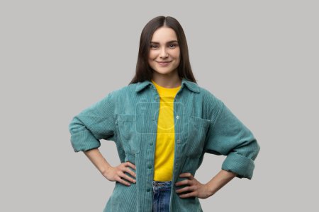 Photo for Portrait of happy optimistic young woman standing with hands on hips looking at camera with charming and toothy smile, wearing casual style jacket. Indoor studio shot isolated on gray background. - Royalty Free Image