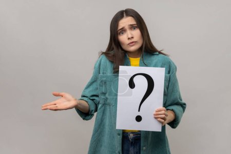 Photo for Portrait of confused puzzled woman looking at camera, holding paper with question mark, thinks about tasks, wearing casual style jacket. Indoor studio shot isolated on gray background. - Royalty Free Image