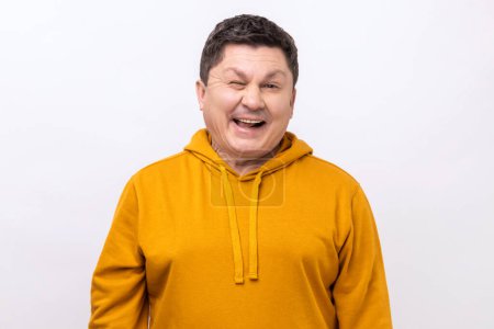 Photo for Happy positive man of middle age winking looking at camera with playful smile, flirting, has good mood, waiting for date, wearing urban style hoodie. Indoor studio shot isolated on white background. - Royalty Free Image
