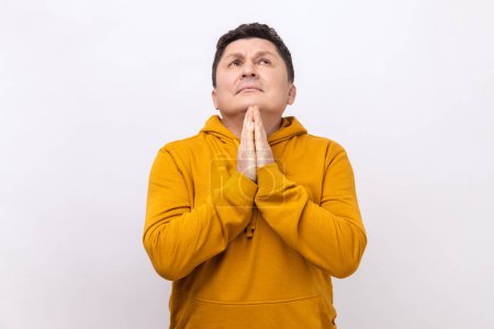 Photo for Portrait of handsome middle aged man praying up heartily, feeling guilty, pleading begging help from heaven, wearing urban style hoodie. Indoor studio shot isolated on white background. - Royalty Free Image