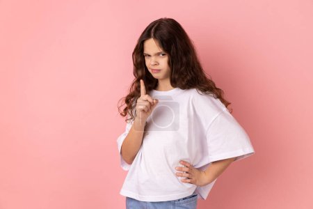 Photo for Hey you, be careful. Portrait of strict bossy little girl wearing white T-shirt seriously pointing finger and looking at camera, warning. Indoor studio shot isolated on pink background. - Royalty Free Image