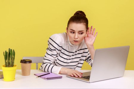 Photo for I can't hear you. Woman holding arm near ear trying to listen secret talk on video call on laptop, bad internet connection, online conference. Indoor studio studio shot isolated on yellow background. - Royalty Free Image