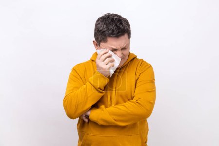 Photo for Depressed desperate middle aged man rubbing tired eyes, crying because of hopelessness and loneliness, nervous breakdown, wearing urban style hoodie. Indoor studio shot isolated on white background. - Royalty Free Image