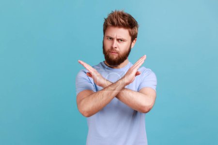 Photo for There is no way. Portrait of concerned disappointed handsome bearded man showing x sign with crossed hands, meaning stop, finish. Indoor studio shot isolated on blue background. - Royalty Free Image