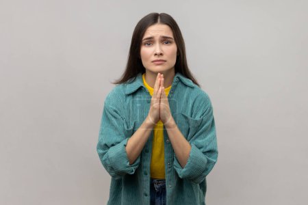 Téléchargez les photos : Please, I'm begging. Desperate woman keeping arms in prayer gesture and asking forgiveness, feeling sorry for mistake, wearing casual style jacket. Indoor studio shot isolated on gray background. - en image libre de droit