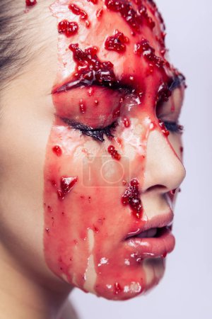 Foto de Side view closeup portrait of woman with jam flowing over her face, model closed her eyes, having serious facial expression. Indoor studio shot isolated on gray background. - Imagen libre de derechos