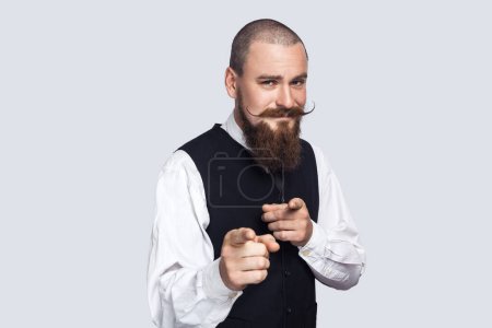 Photo for Portrait of joyful cheerful attractive man with beard and mustache indicating both index fingers at camera, saying he needs you, choosing. Indoor studio shot isolated on gray background. - Royalty Free Image