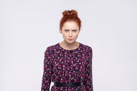 Téléchargez les photos : Portrait of angry unhappy young adult redhead woman wearing dress standing looking at camera, expressing aggression and hate. Indoor studio shot isolated on gray background. - en image libre de droit