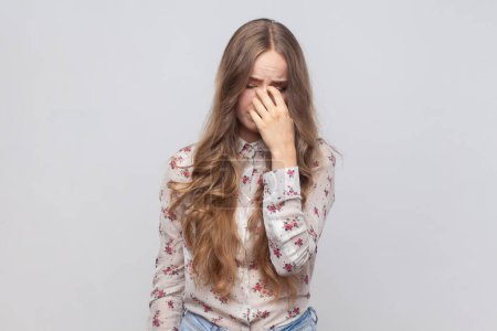 Photo for Portrait of desperate depressed woman with wavy blond hair rubbing eyes, crying because of hopelessness and loneliness, nervous breakdown. Indoor studio shot isolated on gray background. - Royalty Free Image