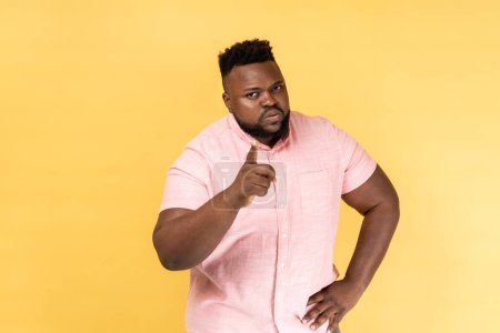 Photo for I told you. Portrait of man wearing pink shirt pointing finger at camera and looking with dissatisfied suspicious expression, warning about troubles. Indoor studio shot isolated on yellow background. - Royalty Free Image