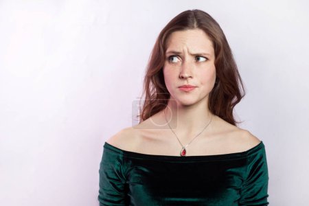 Photo for Portrait of confused puzzled pensive woman wearing green dress looking away with pensive thoughtful expression, thinking about problem. Indoor studio shot isolated on gray background. - Royalty Free Image