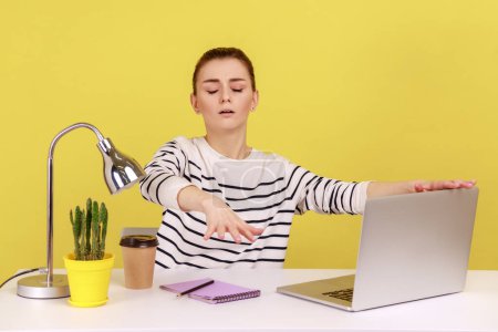 Foto de Disoriented blind woman employee sitting at workplace with laptop and outstretching hands, touching air with attention to senses. Indoor studio studio shot isolated on yellow background. - Imagen libre de derechos