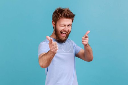 Foto de You are special. Portrait of positive happy bearded man pointing fingers at camera and looking with toothy smile, believes in you, motivation. Indoor studio shot isolated on blue background. - Imagen libre de derechos