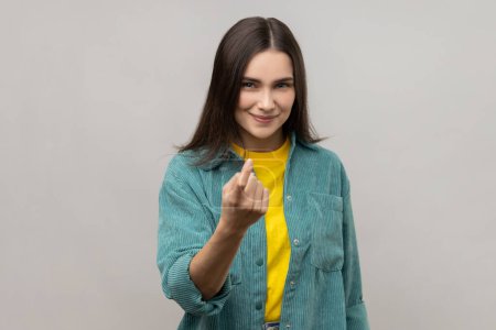 Téléchargez les photos : Come here. Portrait of attractive woman gesturing come to me, beckoning with finger, inviting for confidential talk, wearing casual style jacket. Indoor studio shot isolated on gray background. - en image libre de droit