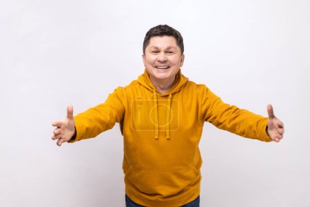 Téléchargez les photos : Free hugs. Portrait of friendly kind man stretching hands to camera and smiling broadly, going to embrace, share love, wearing urban style hoodie. Indoor studio shot isolated on white background. - en image libre de droit