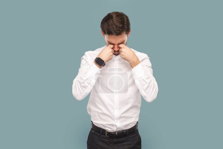 Foto de Portrait of sad depressed crying man with mustache standing and rubbing his eyes, being in bad mood and having stress, wearing Indoor studio shot isolated on light blue background. - Imagen libre de derechos