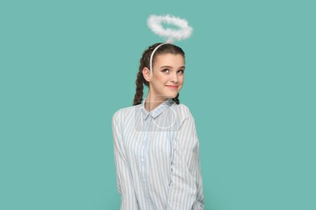 Photo for Portrait of pretty lovely friendly angelic teenager girl with braids wearing striped shirt and nimb over head, coquetry with boyfriend. Indoor studio shot isolated on green background. - Royalty Free Image