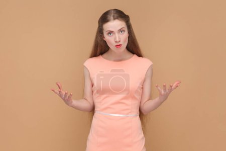 Photo for Portrait of beautiful attractive angry woman with long hair standing with raised arms, arguing, having aggressive expression, wearing elegant dress. Indoor studio shot isolated on brown background. - Royalty Free Image