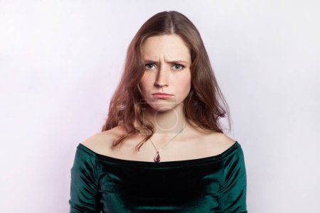 Photo for Portrait of sad worried woman wearing green dress standing looking at camera with pout lips, expressing sorrow and sadness, being offended. Indoor studio shot isolated on gray background. - Royalty Free Image