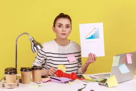Photo for Portrait of serious woman office manager looking at camera showing growth diagram, financial and economic growth of his business. Indoor studio studio shot isolated on yellow background. - Royalty Free Image