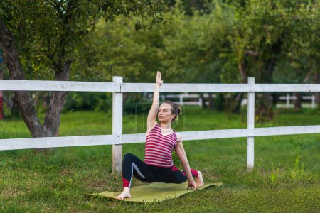 Photo for Full length of motivated fit athletic woman wearing sportswear practicing yoga on mat outdoor in summer day, standing in Virabhadrasana warrior pose and meditating, doing stretching exercise. - Royalty Free Image