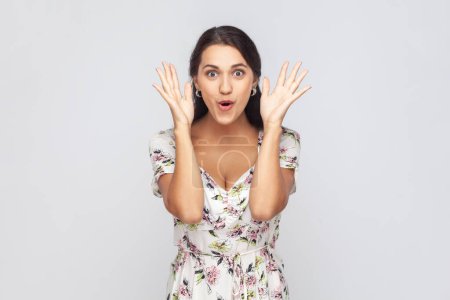 Photo for Portrait of astonished woman wearing white dress standing with mouth open in surprise, has shocked expression, hears unbelievable news, raised hands. Indoor studio shot isolated on gray background. - Royalty Free Image