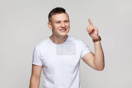 Photo for Eureka. Portrait of handsome excited inspired teenager boy wearing T-shirt standing with raised finger, having an excellent idea, smiling. Indoor studio shot isolated on gray background. - Royalty Free Image