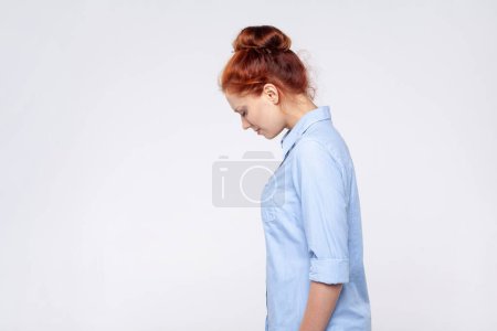 Photo for Side view portrait of sad upset redhead woman wearing blue shirt crying with sorrow, feeling lonely hopeless, desperate emotions, worried about troubles. Indoor studio shot isolated on gray background - Royalty Free Image