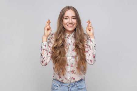 Photo for Portrait of hopeful joyous beautiful young adult woman with wavy blond hair raising fingers crossed while making wish, confident to win. Indoor studio shot isolated on gray background. - Royalty Free Image