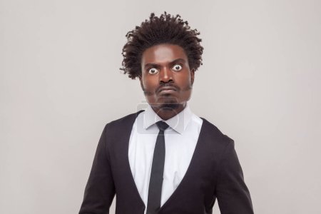 Photo for Portrait of man with Afro hairstyle looks with angry strict expression gazes directly at camera, has negative emotions, wearing white shirt and tuxedo. Indoor studio shot isolated on gray background. - Royalty Free Image