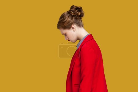 Photo for Side view portrait of worried stressed woman with red lips standing looking at camera with sad expression, feels upset, wearing red jacket. Indoor studio shot isolated on yellow background. - Royalty Free Image