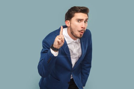 Photo for Portrait of amazed clever smart man with mustache standing with raised finger, having excellent idea, wearing white shirt and jacket. Indoor studio shot isolated on light blue background. - Royalty Free Image