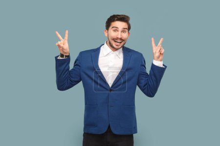 Photo for Delighted man with mustache standing ,with v signs, looking at camera with positive facial expression, wearing white shirt and jacket. Indoor studio shot isolated on light blue background. - Royalty Free Image