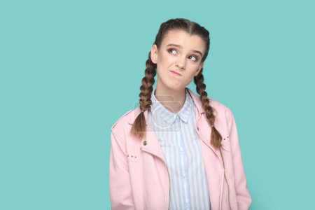 Photo for Portrait of pensive thoughtful young teenager girl with braids wearing pink jacket looking away with puzzled confused expression. Indoor studio shot isolated on green background. - Royalty Free Image
