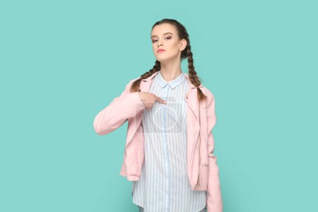 Photo for Portrait of self-confident proud teenager girl with braids wearing pink jacket pointing at herself with pride, having egoistic expression. Indoor studio shot isolated on green background. - Royalty Free Image