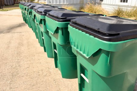 Téléchargez les photos : Gros plan de la rangée de poubelles vertes et propres près de la maison, élimination des ordures dans des conteneurs verts dans un complexe résidentiel. - en image libre de droit