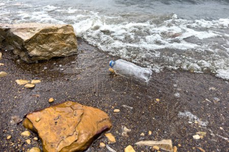 Foto de Derramó basura en la playa vacía utiliza botella de plástico sucio, costa arenosa del mar sucio, contaminación ambiental, problema ecológico, olas en movimiento en el fondo. - Imagen libre de derechos