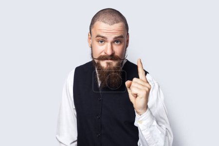 Photo for Portrait of excited clever man with beard and mustache standing with raised finger, having excellent idea, looks smart and inspired. Indoor studio shot isolated on gray background. - Royalty Free Image