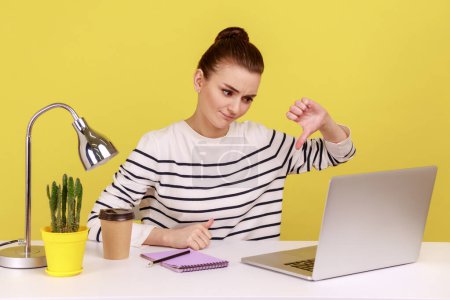 Photo for Displeased woman office worker showing thumbs down to laptop monitor while having video call, dislike gesture, expressing disapproval. Indoor studio studio shot isolated on yellow background. - Royalty Free Image