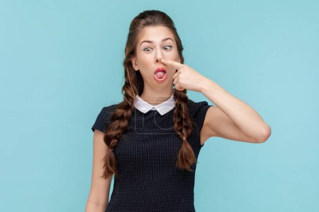 Photo for Funny impolite woman with braids making crazy face with tongue out and picking her nose, bad manners, sticking tongue, wearing black dress. woman Indoor studio shot isolated on blue background. - Royalty Free Image