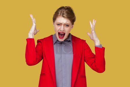 Photo for Portrait of annoyed crazy woman with red lips standing with raised arms and screaming loud, having trouble, feels nervous, wearing red jacket. Indoor studio shot isolated on yellow background. - Royalty Free Image