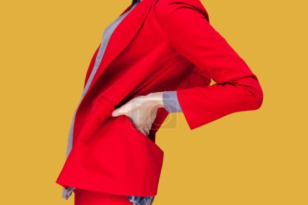 Photo for Side view portrait of unknown sick unhealthy woman standing touching her painful back, feels kidney pain, wearing red jacket. Indoor studio shot isolated on yellow background. - Royalty Free Image