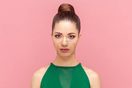 Photo for Portrait of serious strict young adult woman standing looking at camera with concentrated expression, being in bad mood, wearing green dress. Indoor studio shot isolated on pink background. - Royalty Free Image