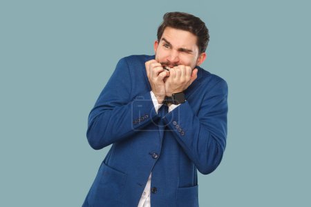 Photo for Portrait of nervous depressed man with mustache standing biting his fingernails, being worried, frowning face, wearing official style suit. Indoor studio shot isolated on light blue background. - Royalty Free Image