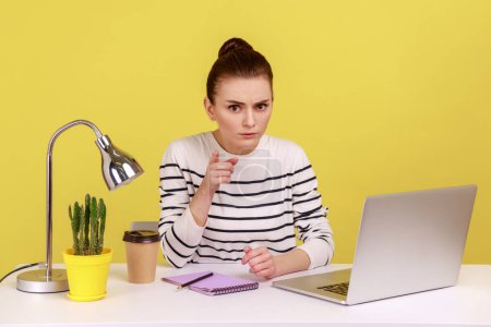 Photo for Portrait of serious woman office employee wearing striped shirt sitting on workplace, scolding, saying I have told you, looking at camera. Indoor studio studio shot isolated on yellow background. - Royalty Free Image