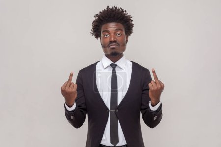 Photo for Impolite displeased man with Afro hairstyle shows middle finger, being angry with someone, purses lips frowns furious, wearing white shirt and tuxedo. Indoor studio shot isolated on gray background. - Royalty Free Image