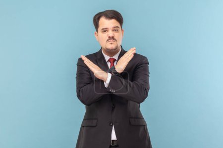 Photo for Portrait of angry upset man with mustache standing standing with crossed arms, saying no way, warning, wearing black suit with red tie. Indoor studio shot isolated on light blue background. - Royalty Free Image