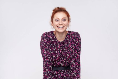 Photo for Portrait of extremely happy optimistic redhead woman wearing dress looking at camera with toothy smile, rejoicing, being in good mood. Indoor studio shot isolated on gray background. - Royalty Free Image