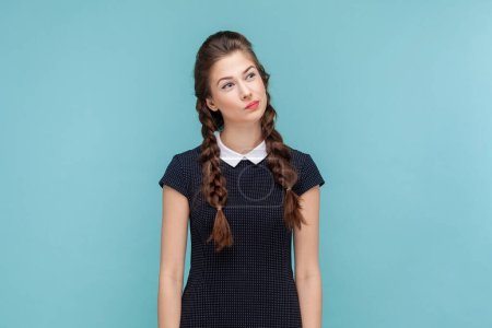 Photo for Portrait of pensive thoughtful woman with braids standing and looking away, making decision, thinks about solving problem, wearing black dress. woman Indoor studio shot isolated on blue background. - Royalty Free Image